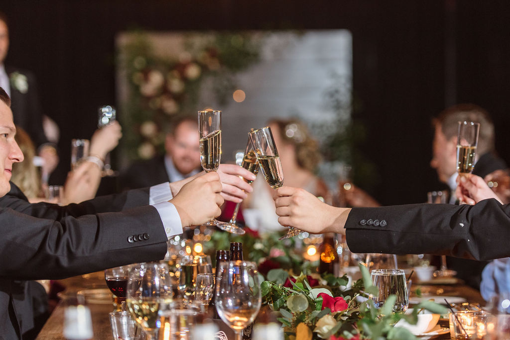 Guests reach across a long dining table inside the High Line Car House to cheers with champagne glasses.