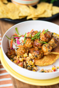 A closeup of Sweet Carrot's Ohio Chicken Meatballs in a white bowl on Corn Cakes topped with Corn Salsa