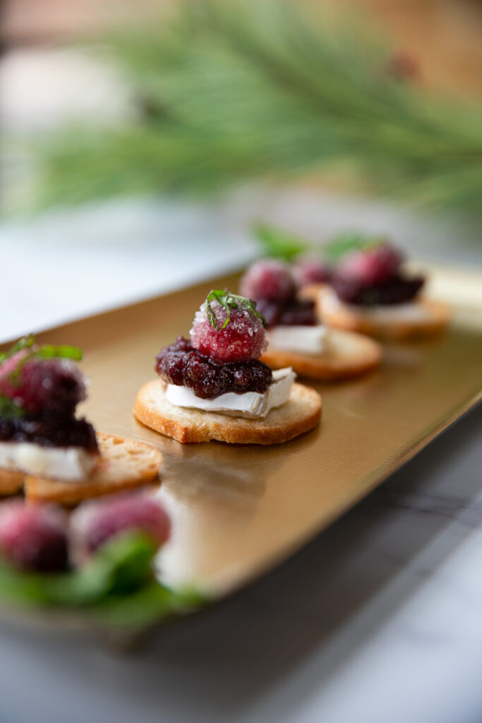 A lineup of winter hors d'oeuvres sit on a long gold plate. There is greenery out of focus in the backround