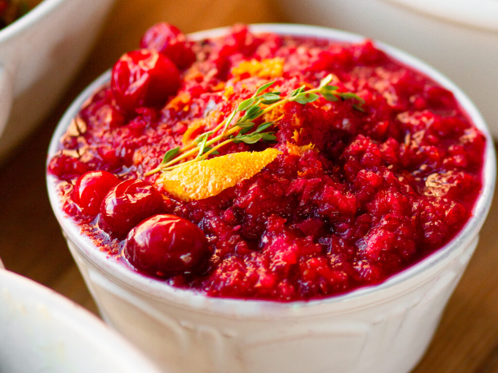 A closeup of our Cranberry-Orange Relish in a white bowl with a thyme and orange zest garnish.
