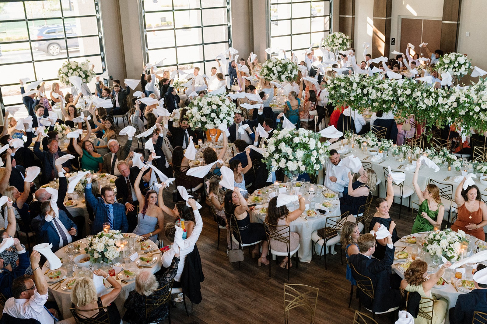 Wedding guests wave napkins in the air as they take their seats for a reception dinner