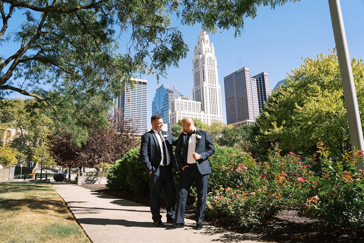 Two grooms stand together in front of the Columbus skyline