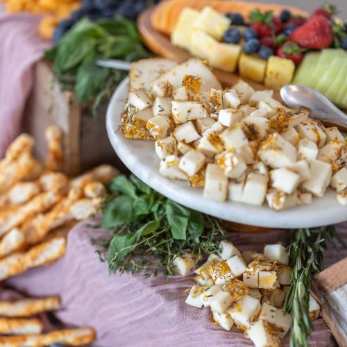 An abundant display of artisan cheeses, dried fruit, and herbs at a summer party.