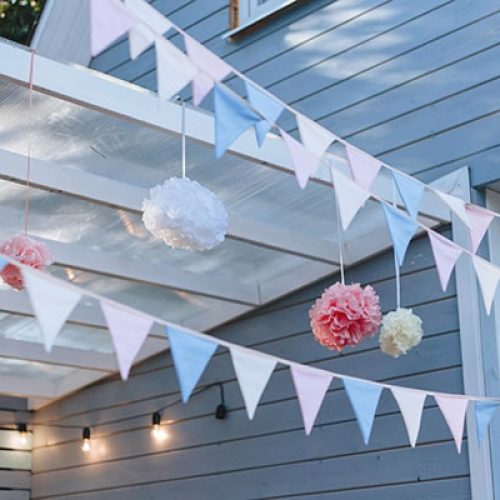 Pennant banners, cafe lights, and tissue paper decor hang over an outdoor patio at a private residence.