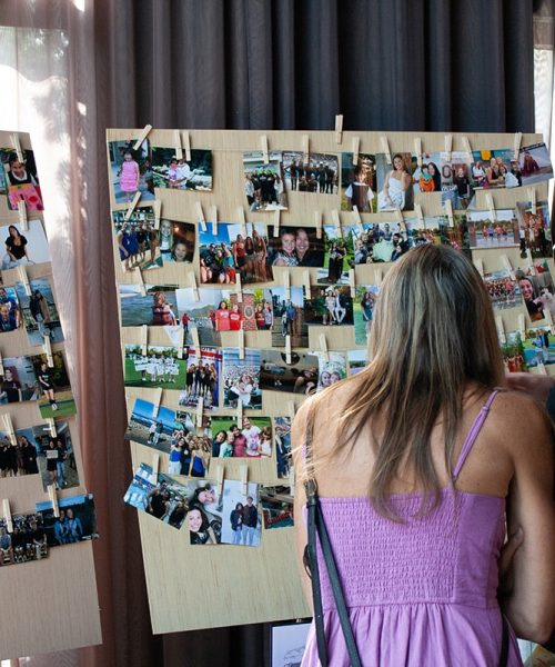 A couple of guests stand in front of a photo collage at their classmate’s graduation party.